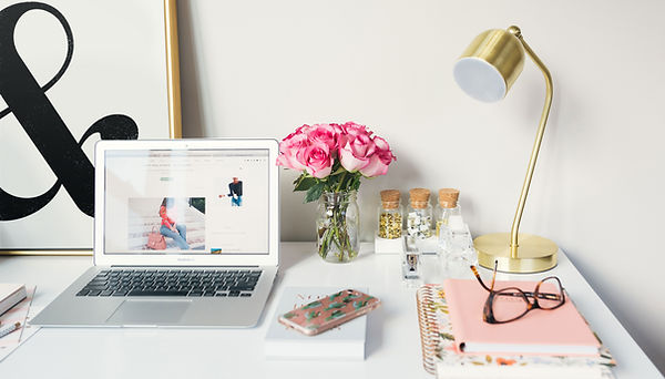 Work Station wih a laptop, phone, notebooks, lamp and glasses and pink flowers in a vase.