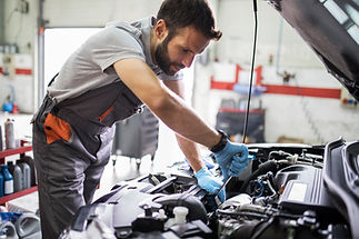 A mechanic in a garage servicing a car engine while wearing blue gloves