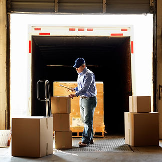 Worker standing at the rear of a delivery truck while reviewing a warehouse shipment