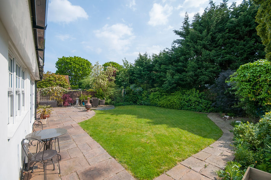 A back garden features a curved, grassy lawn surrounded by lush bushes
