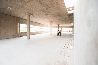 Two men with plan wearing safety vests talking in building under construction