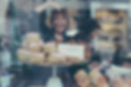 cake shop window displaying sugary treats and reflections of happy people looking at cakes 