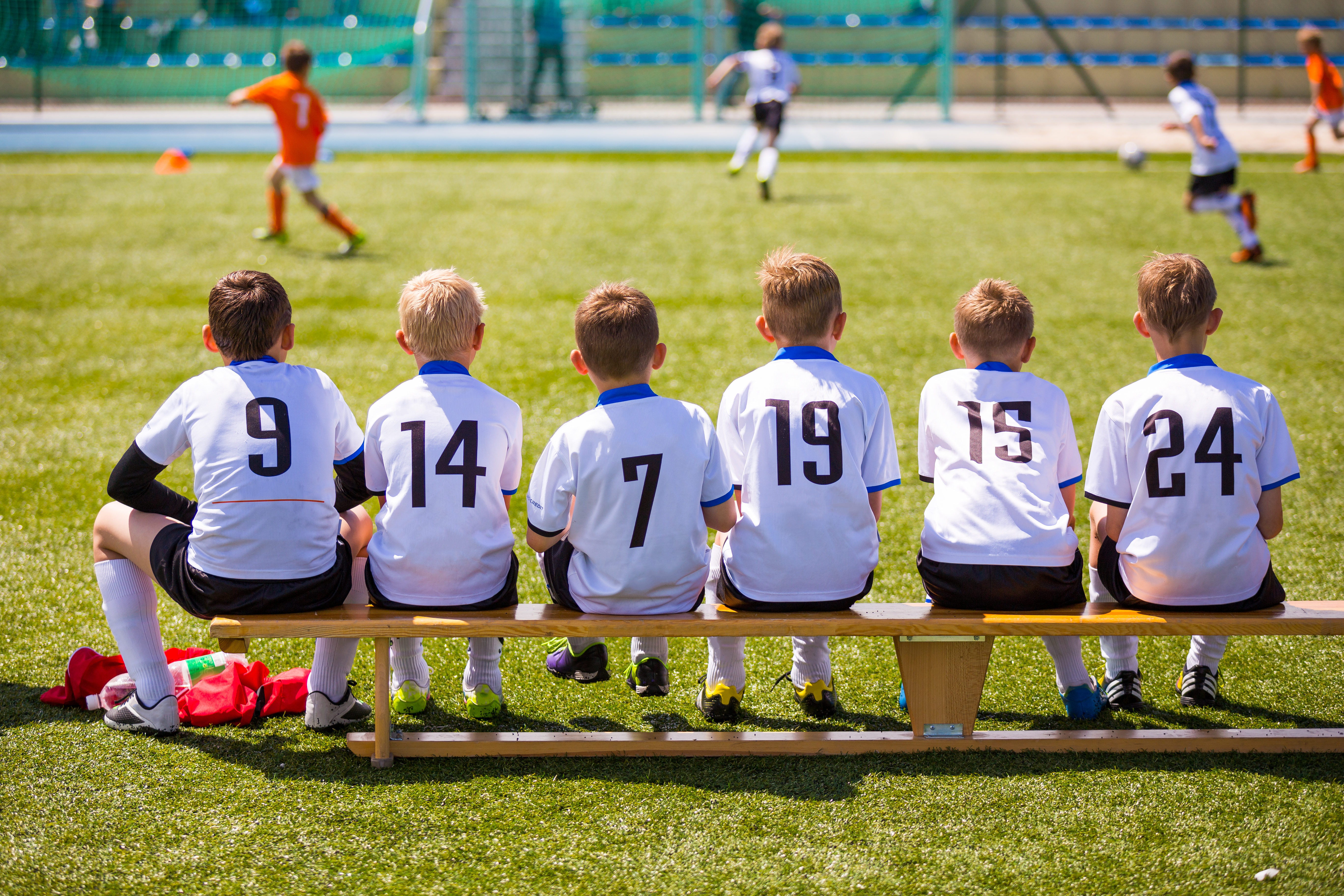 Young football players seated on the bench, eagerly watching their teammates in action during a grassroots match.