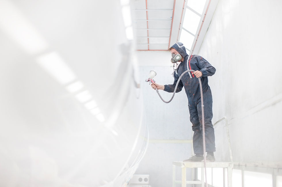 Painter wearing protective suit and respirator mask spray painting a large surface in a spray booth.
