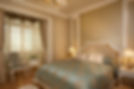 A master bedroom featuring a large tufted cream headboard and elegant wallpaper