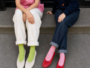 Two people sit on concrete steps, wearing pink gingham and navy outfits with bright socks and flats, a casual colorful scene.