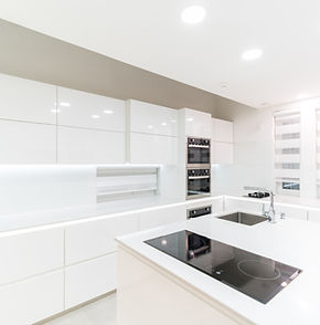 A modern, minimalist kitchen with sleek white cabinets, black stovetop