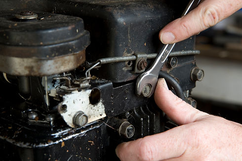 A pair of hands using a spanner to adjust a bolt on a small engine