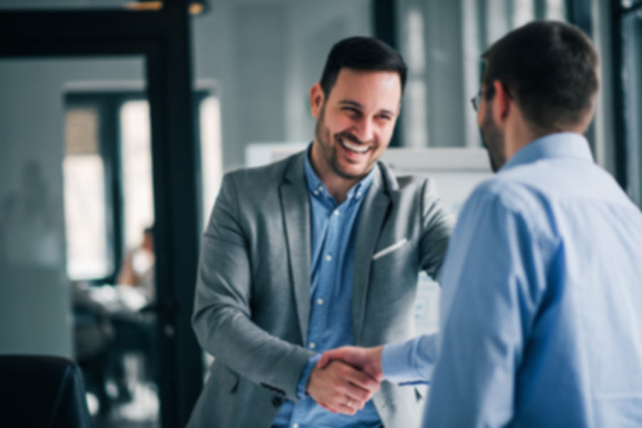 Two professionals are smiling and shaking hands in an office space.