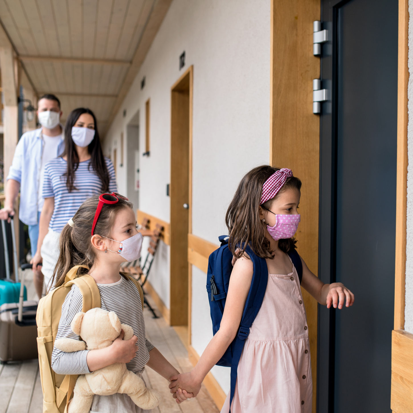 Family wearing masks entering a hotel room with luggage