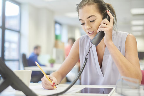 a young woman in a casual modern office chats to a client on the phone whilst using her di