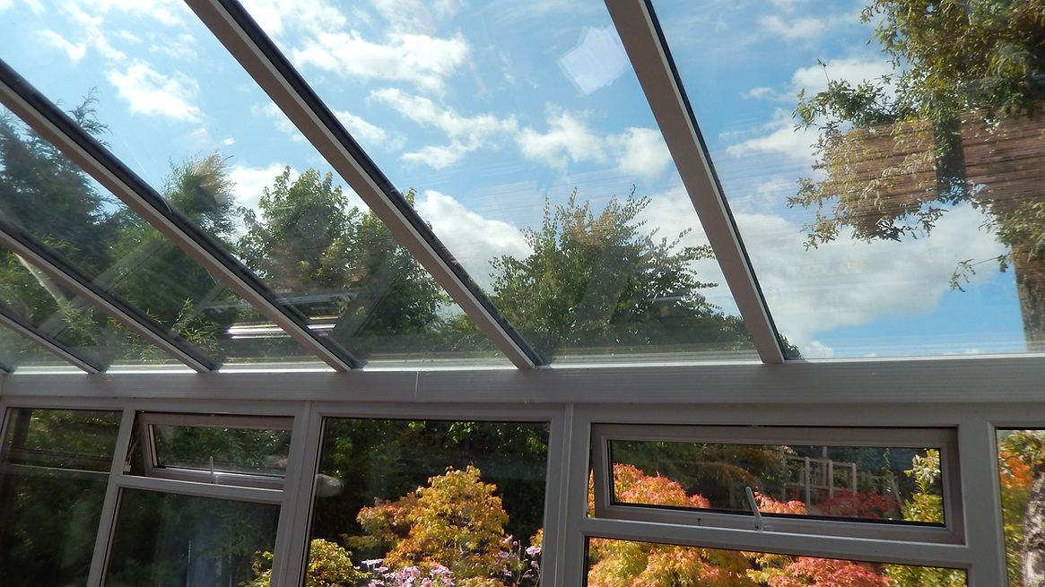 View through a glass conservatory roof showing a bright blue sky with scattered clouds