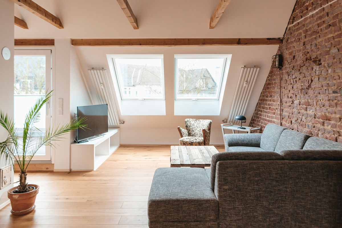 Rustic attic lounge with beams, brick wall and grey sectional