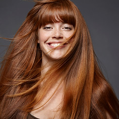 Young woman with long flowing red hair and fringe smiling at camera