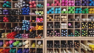 Organized display of colorful pens and markers in a wooden shelf, showcasing a variety of hues. Labels visible on some pen caps.