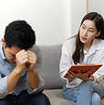 A man and woman are seated on a couch, absorbed in reading a book together.