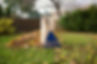 A yard rake leaning on a paper leaf bag amidst fallen leaves with a wooden fence