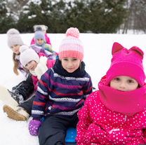 Children in colorful winter gear, sitting on a sled in the snow. Trees in the background. Joyful and playful winter scene.
