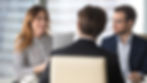 Professional financial advisor meeting with two clients in a modern office, reviewing documents and discussing a financial plan.