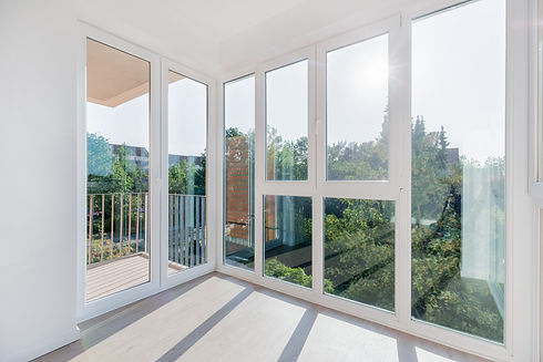 Bright room with large floor-to-ceiling windows, overlooking a sunny balcony and lush green trees