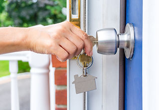 Hand inserting a silver key into a modern metal door handle lock