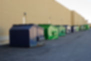 Blue and green industrial waste bins lined up outside the commercial building