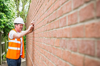 Caucasian construction worker in orange high-vis vest and hard hat holding a string line against a red brick wall