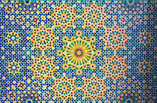 An intricate geometric mosaic tile pattern features a central starburst with vibrant blue, yellow, and green star motifs