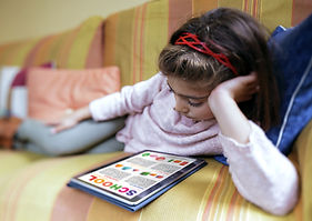Girl relaxing on couch, reading 'SCHOOL' tablet app