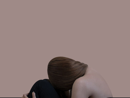 Person sitting curled inward with head down, illustrating how emotional triggers trauma can cause intense reactions to everyday situations.