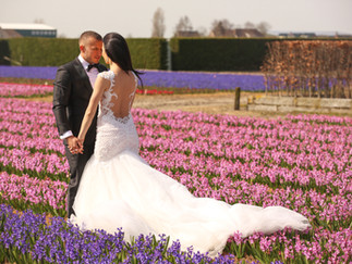 Bride and groom stood in a flower field holding hands facing each other