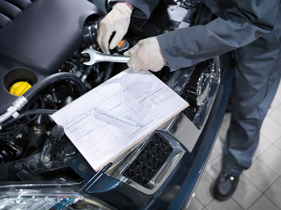Mechanic's hands holding tool and inspecting car engine in car dealership workshop
