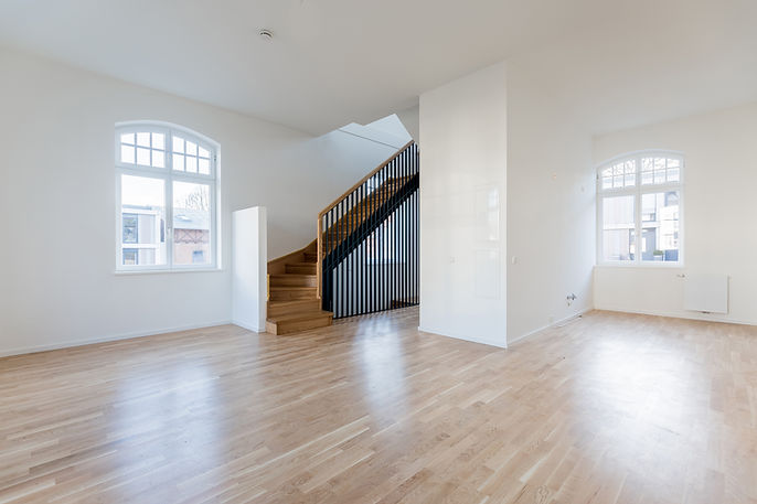 Bright empty interior of a refurbished building featuring white walls and a central timber staircase