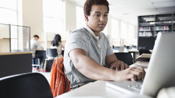 Young man working on a laptop at a library desk study tools