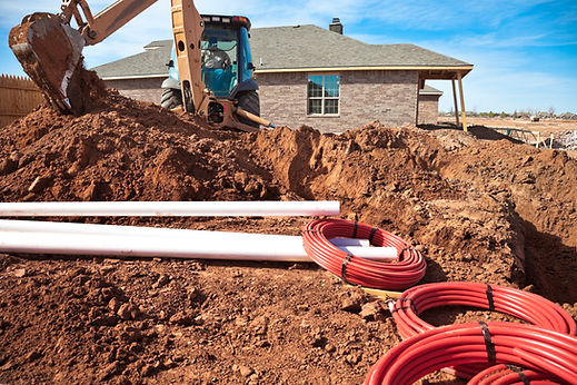 Tractor digger working on a dirt trench next to a house with pipes ready