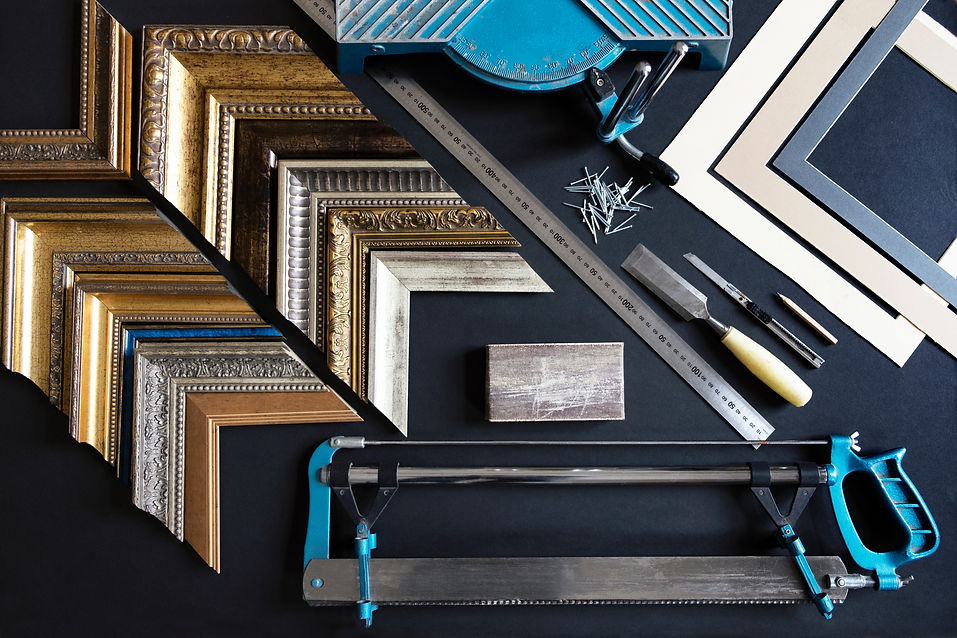 Various ornate picture frames in gold, silver, and wood are arranged on a black table
