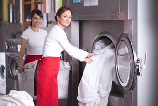 Two workers in laundry service,get washed sheets out of washing machine