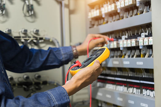 Electrician holding multimeter during electrical control panel's inspection