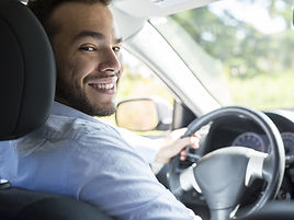 Foto de um motorista sorridente e profissional da LiberwayUSA, olhando para o banco dos passageiros enquanto se apresenta e d