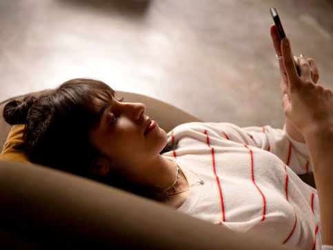 A young adult lying on her couch looking up at her mobile phone