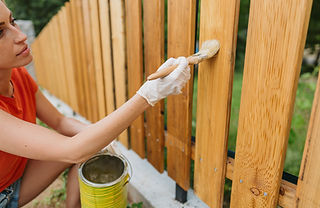 Photo of a young woman painting a picket fence