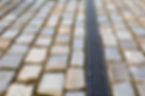 Close-up of grey cobblestone pavement with a black metal drainage grate running vertically