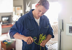 A man in a blue jumpsuit carefully works with green electrical wires in a modern room