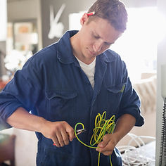 A man in a blue jumpsuit carefully works with green electrical wires in a modern room