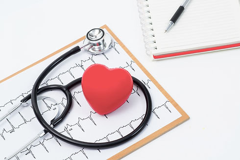 Medical stethoscope head and red toy heart lying on cardiogram chart closeup
