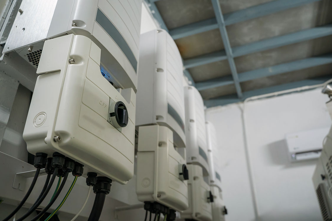 Row of white electrical inverters in an industrial setting, mounted on a wall