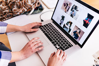 A person's hands using a laptop displaying an online clothing store.