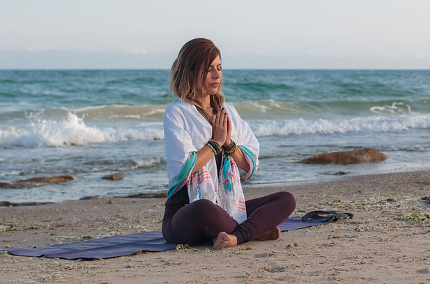 Women meditating with hands in pray on a breach with the waves behind