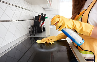 A person in yellow gloves cleans a kitchen stovetop with a spray and cloth