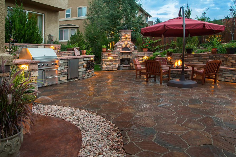 A large patio with an outdoor kitchen and a brick fireplace